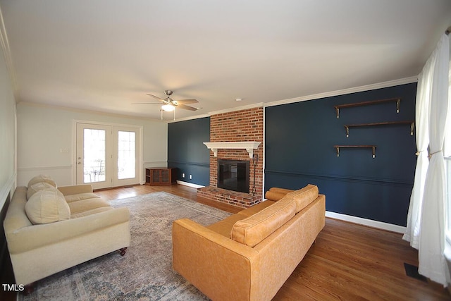 living area featuring wood finished floors, a fireplace, crown molding, baseboards, and ceiling fan