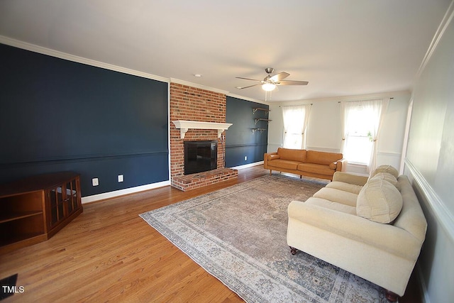 living area with a brick fireplace, wood finished floors, ceiling fan, and ornamental molding