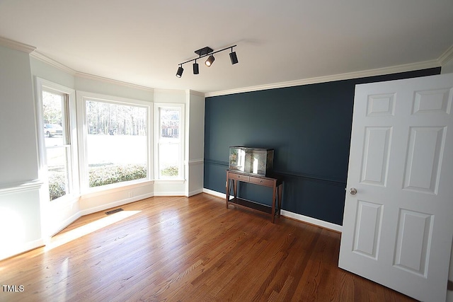 spare room with visible vents, track lighting, wood finished floors, crown molding, and baseboards