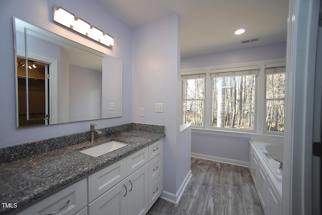 bathroom featuring vanity, wood finished floors, visible vents, baseboards, and a bath