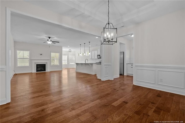 unfurnished living room featuring a ceiling fan, dark wood-style floors, a wainscoted wall, a tray ceiling, and a fireplace