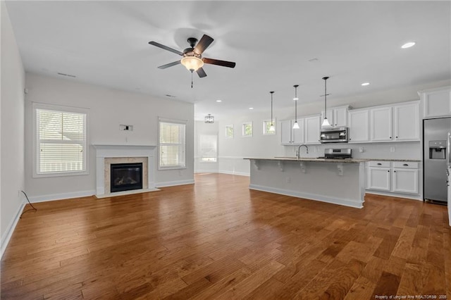 kitchen featuring open floor plan, appliances with stainless steel finishes, a kitchen breakfast bar, wood finished floors, and white cabinets