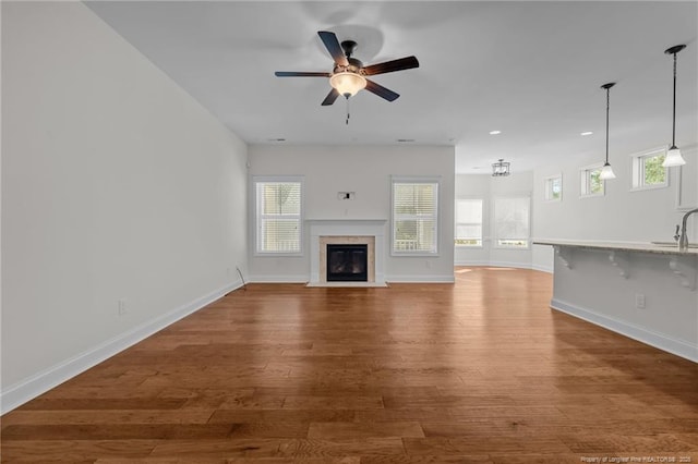 unfurnished living room featuring a fireplace, wood finished floors, baseboards, and a sink