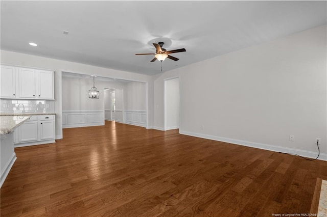 unfurnished living room featuring dark wood finished floors, ceiling fan with notable chandelier, and baseboards