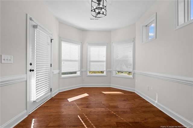 unfurnished dining area with dark wood finished floors, visible vents, a notable chandelier, and baseboards