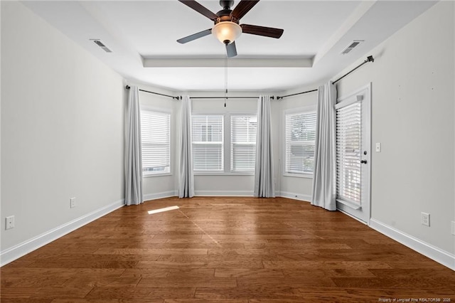 unfurnished room with a tray ceiling, baseboards, visible vents, and wood finished floors