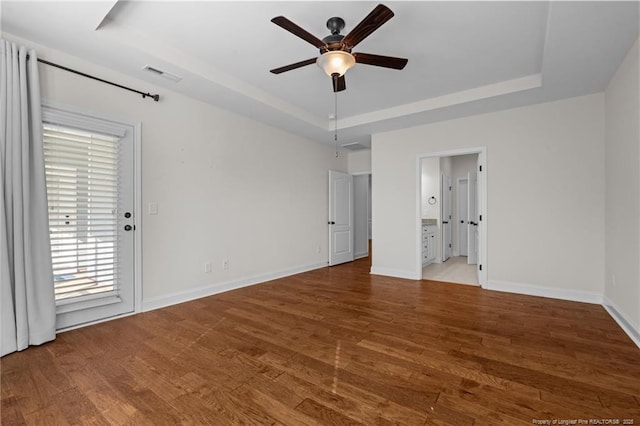 unfurnished bedroom featuring visible vents, a raised ceiling, baseboards, and wood finished floors