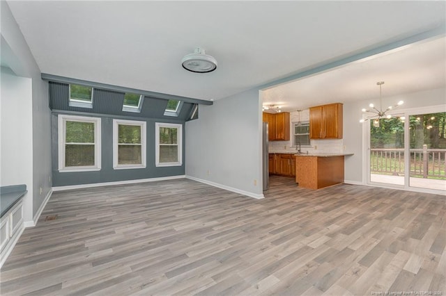 unfurnished living room featuring baseboards, an inviting chandelier, and light wood finished floors