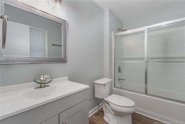 bathroom with vanity, wood finished floors, baseboards, toilet, and combined bath / shower with glass door