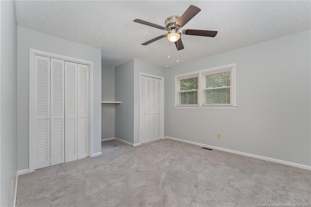 unfurnished bedroom featuring carpet, visible vents, two closets, and baseboards