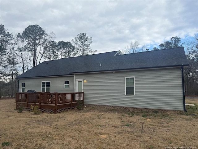 back of property with a deck, a lawn, and a shingled roof