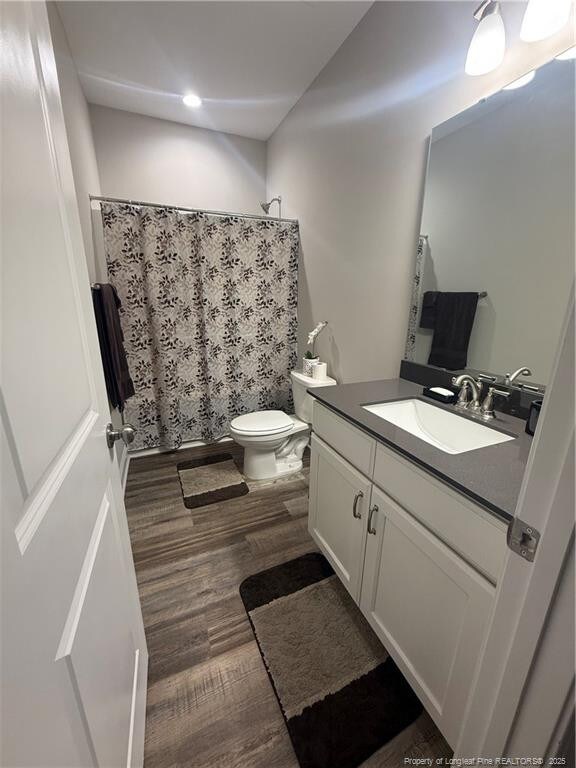 full bath featuring vanity, a shower with shower curtain, toilet, and wood finished floors