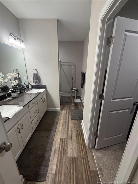 full bathroom with wood finished floors, baseboards, double vanity, a sink, and a shower