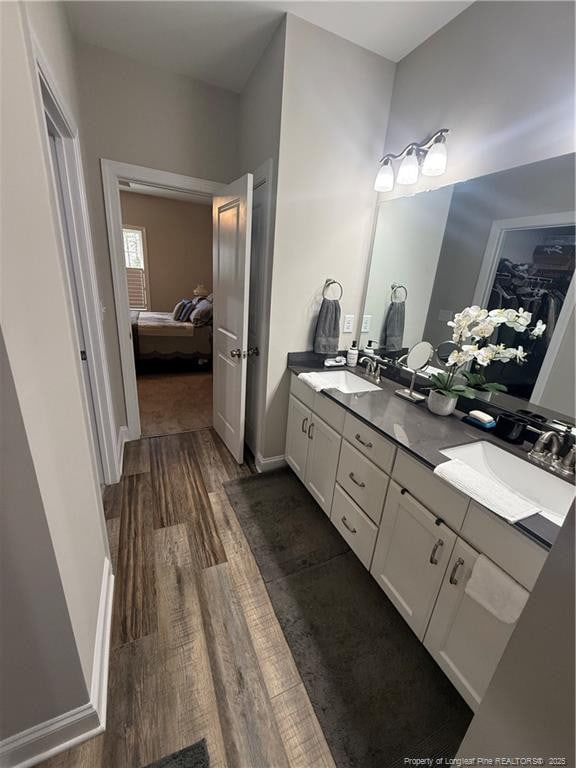 ensuite bathroom featuring ensuite bath, double vanity, wood finished floors, and a sink