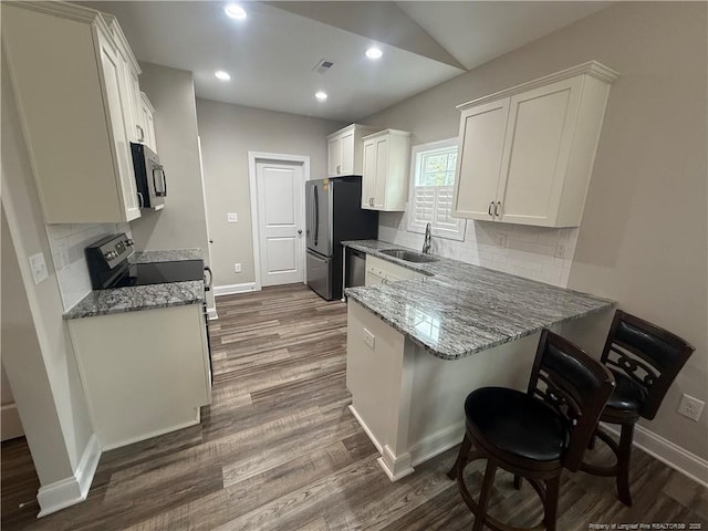 kitchen featuring visible vents, a sink, appliances with stainless steel finishes, a peninsula, and dark wood-style flooring