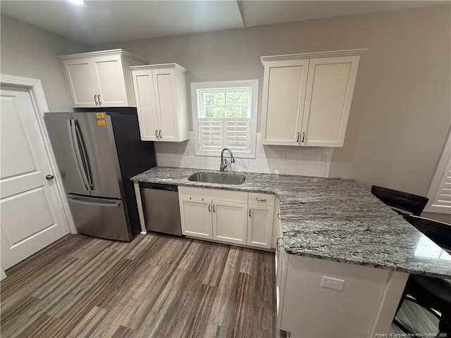 kitchen with appliances with stainless steel finishes, a peninsula, dark wood-style floors, white cabinets, and a sink