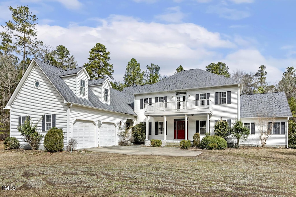 colonial inspired home featuring a porch, roof with shingles, concrete driveway, an attached garage, and a balcony