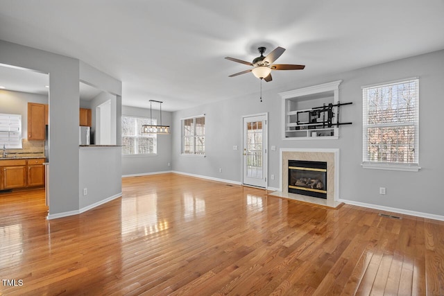 unfurnished living room featuring visible vents, a healthy amount of sunlight, a premium fireplace, and light wood finished floors