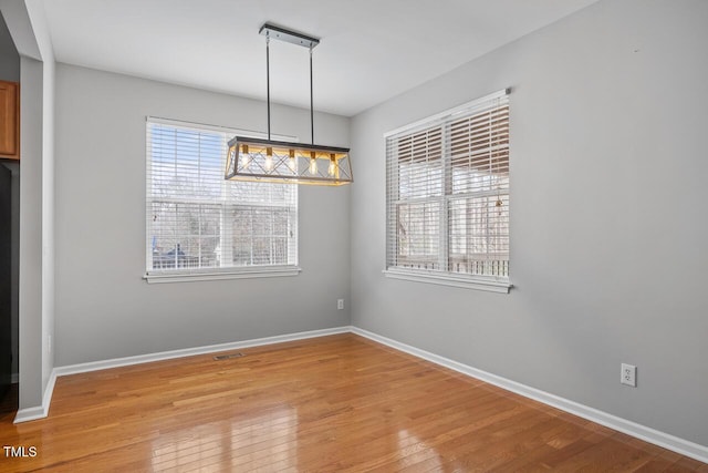 unfurnished dining area with plenty of natural light, light wood-style flooring, visible vents, and baseboards