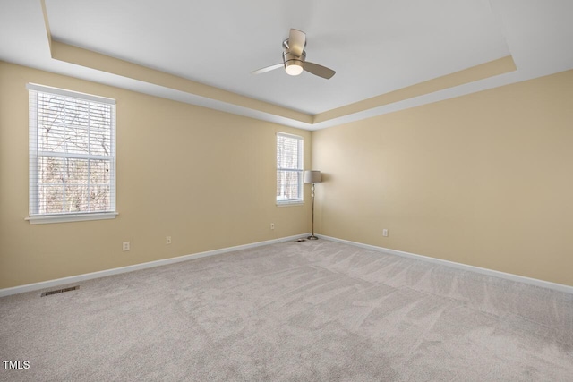 empty room featuring a tray ceiling, light carpet, and a ceiling fan