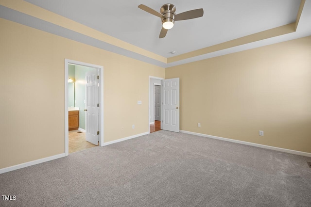 unfurnished bedroom featuring ceiling fan, baseboards, carpet flooring, ensuite bathroom, and a raised ceiling