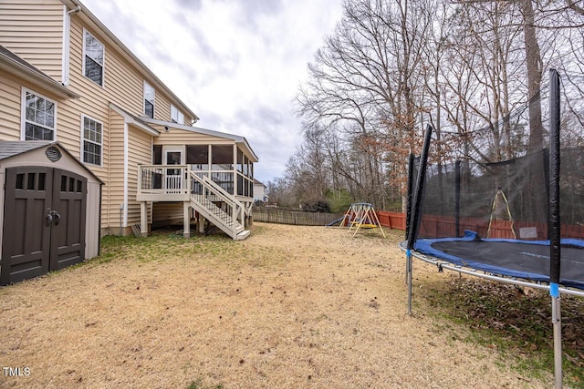 view of yard with a storage unit, a trampoline, a fenced backyard, an outdoor structure, and a sunroom