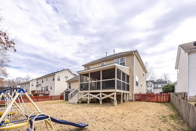 rear view of house featuring a playground, a fenced backyard, and a sunroom