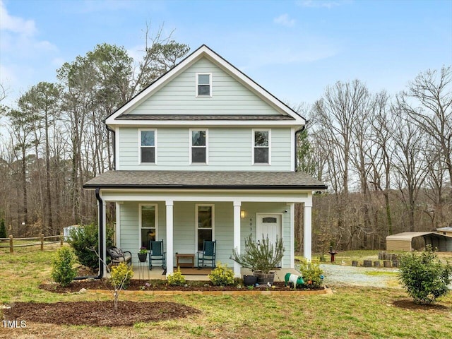 view of front facade with a front yard, fence, covered porch, and roof with shingles