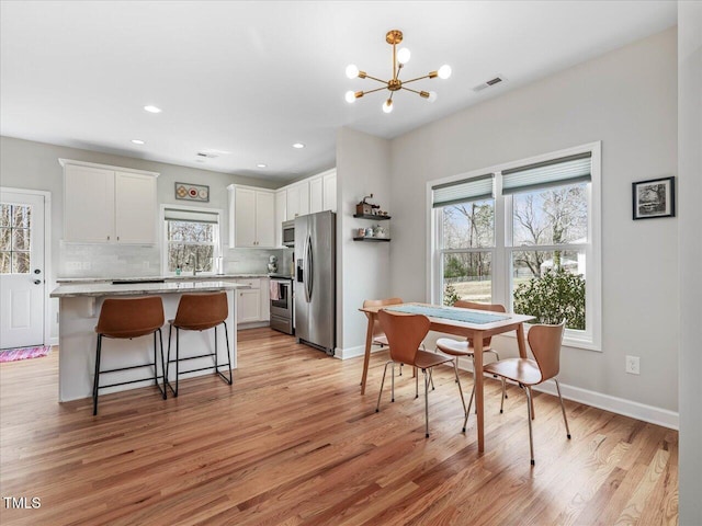 dining space featuring a notable chandelier, baseboards, light wood-type flooring, and visible vents