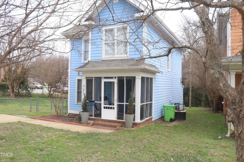 rear view of house featuring a lawn, fence, a sunroom, and a shingled roof