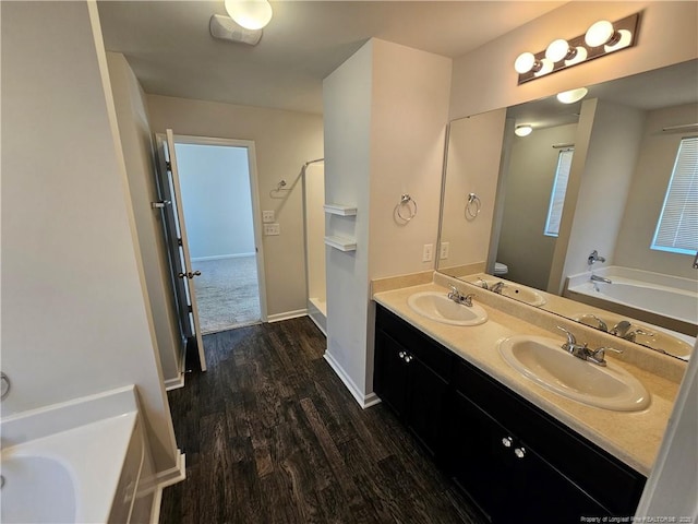 full bath featuring double vanity, wood finished floors, a garden tub, and a sink