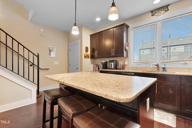 kitchen with dark wood-style floors, a kitchen island, a sink, dark brown cabinetry, and a kitchen bar