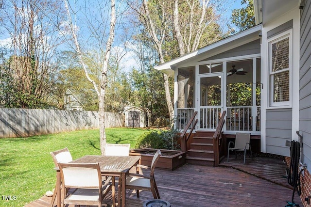 deck featuring outdoor dining space, fence, a shed, an outdoor structure, and a sunroom