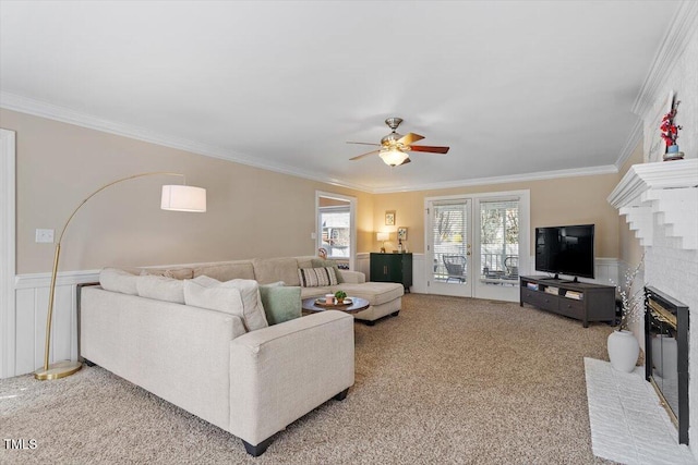 carpeted living area featuring wainscoting, a fireplace, ceiling fan, and ornamental molding