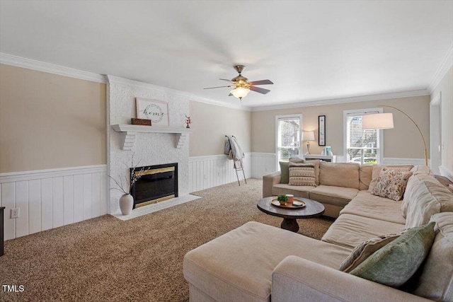 living area with carpet floors, ceiling fan, wainscoting, crown molding, and a brick fireplace