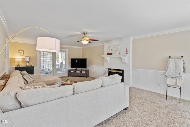 carpeted living area with a ceiling fan, a fireplace, a wainscoted wall, and ornamental molding