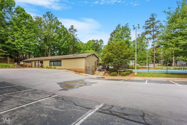 exterior space featuring brick siding, uncovered parking, a tennis court, and fence