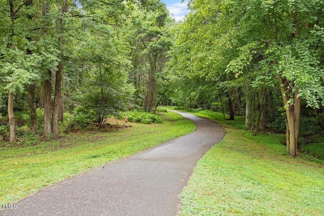 view of community featuring a forest view, aphalt driveway, and a yard