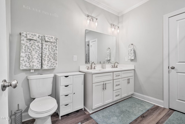 bathroom with wood finished floors, baseboards, a sink, crown molding, and toilet