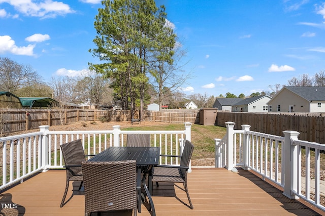 wooden terrace with a residential view, outdoor dining area, a fenced backyard, an outbuilding, and a storage unit