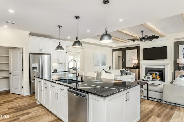 kitchen with light wood finished floors, a sink, open floor plan, stainless steel appliances, and a kitchen island with sink