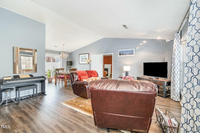 living area with an inviting chandelier, vaulted ceiling, wood finished floors, and visible vents