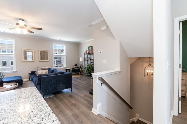 living room featuring ceiling fan with notable chandelier, crown molding, baseboards, and wood finished floors