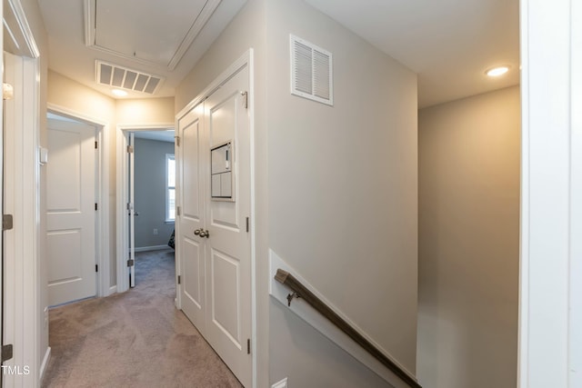 hall with visible vents, light colored carpet, attic access, and baseboards