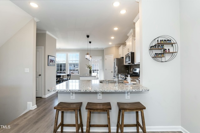 kitchen with a kitchen breakfast bar, appliances with stainless steel finishes, a peninsula, and white cabinetry