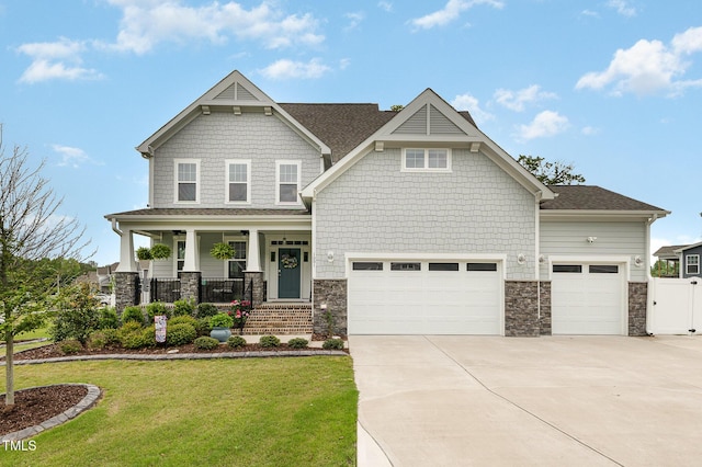 craftsman-style home with fence, a porch, a front lawn, concrete driveway, and stone siding