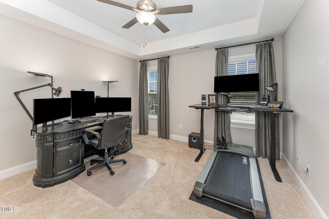 carpeted office space with a raised ceiling, a ceiling fan, visible vents, and baseboards