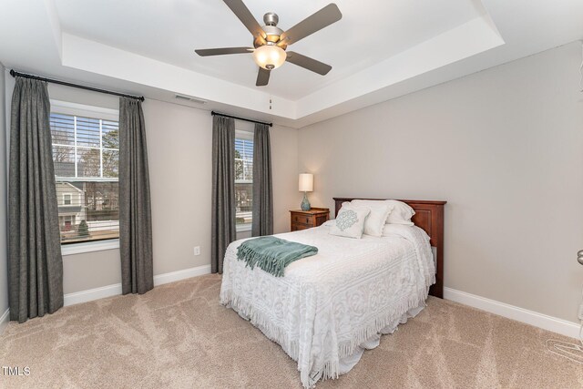 bedroom featuring visible vents, baseboards, ceiling fan, light colored carpet, and a tray ceiling