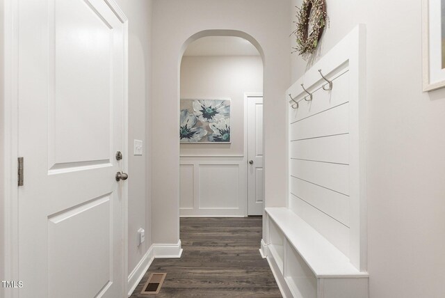 mudroom with dark wood finished floors, a decorative wall, arched walkways, and visible vents