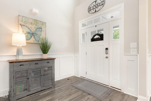 entrance foyer with dark wood finished floors, a decorative wall, visible vents, and a wainscoted wall